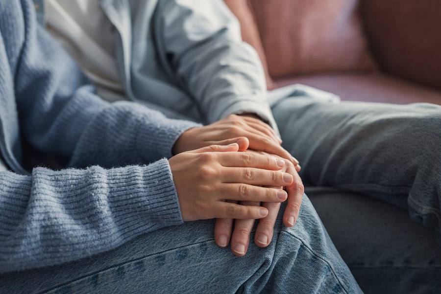 Nahaufnahme zweier Hände, die einer Person auf dem Sofa beruhigend Halt geben.
